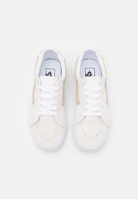 Baskets beige clair avec une tige en daim, des lacets blancs et une semelle en caoutchouc. Elles présentent un embout perforé et des accents couleur tan sur les côtés.