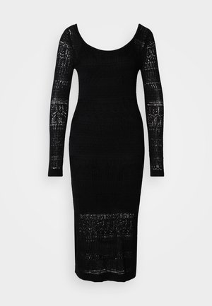 Schwarzes Strickkleid mit langen Ärmeln, weitem Ausschnitt, figurbetontem Schnitt und Durchbrüchen entlang des Oberkörpers und der Ärmel.