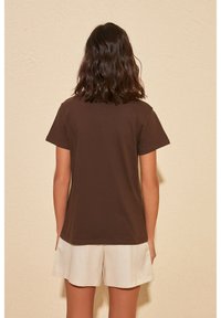 Brun bomull t-shirt med korta ärmar, rund halsringning och en avslappnad passform, i kombination med ljusbeiga shorts. Mjuk textur och enkel design.