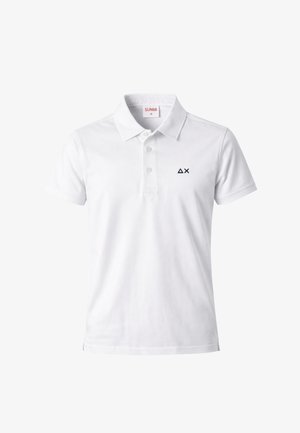 Polo bianca a maniche corte con tre bottoni e piccolo logo nero a triangolo con "X" sul lato sinistro del petto.