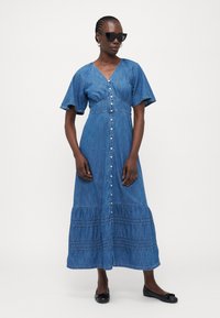 Vestido largo de mezclilla con mangas cortas y acampanadas, escote en V, cierre de botones y falda en capas. Color azul claro con sutiles detalles de costura.
