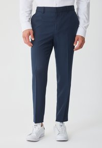 Στενά, σκούρα μπλε παντελόνια με λεία υφή και επίπεδο μπροστινό μέρος. Φορεμένα με λευκά αθλητικά παπούτσια, παρουσιάζοντας ένα μοντέρνο casual στυλ.