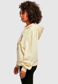 Világos sárga kapucnis pulóver elülső grafikai dizájnnal, színes árnyalatokkal. Puha szövet, laza fazon és oversized ujjakkal.