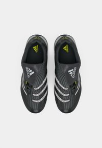 Crne sportske tenisice sa aerodinamičnim dizajnom, teksturiranim gornjim dijelom, srebrnim detaljima i zelenim logotipom na tamnom potplatu. Model na navlačenje s podstavljenim jezikom.