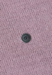 Tissu tricoté en rose doux, présentant un bouton rond noir avec texte gravé et logo au centre, mettant en valeur la texture et les détails.