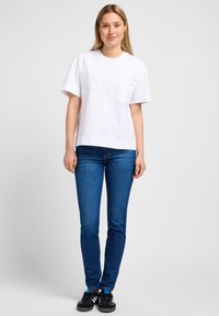 Vit bomull T-shirt med kort ärm och bröstficka, kombinerad med mörkblå slim fit-jeans och svarta sneakers med blå detaljer.