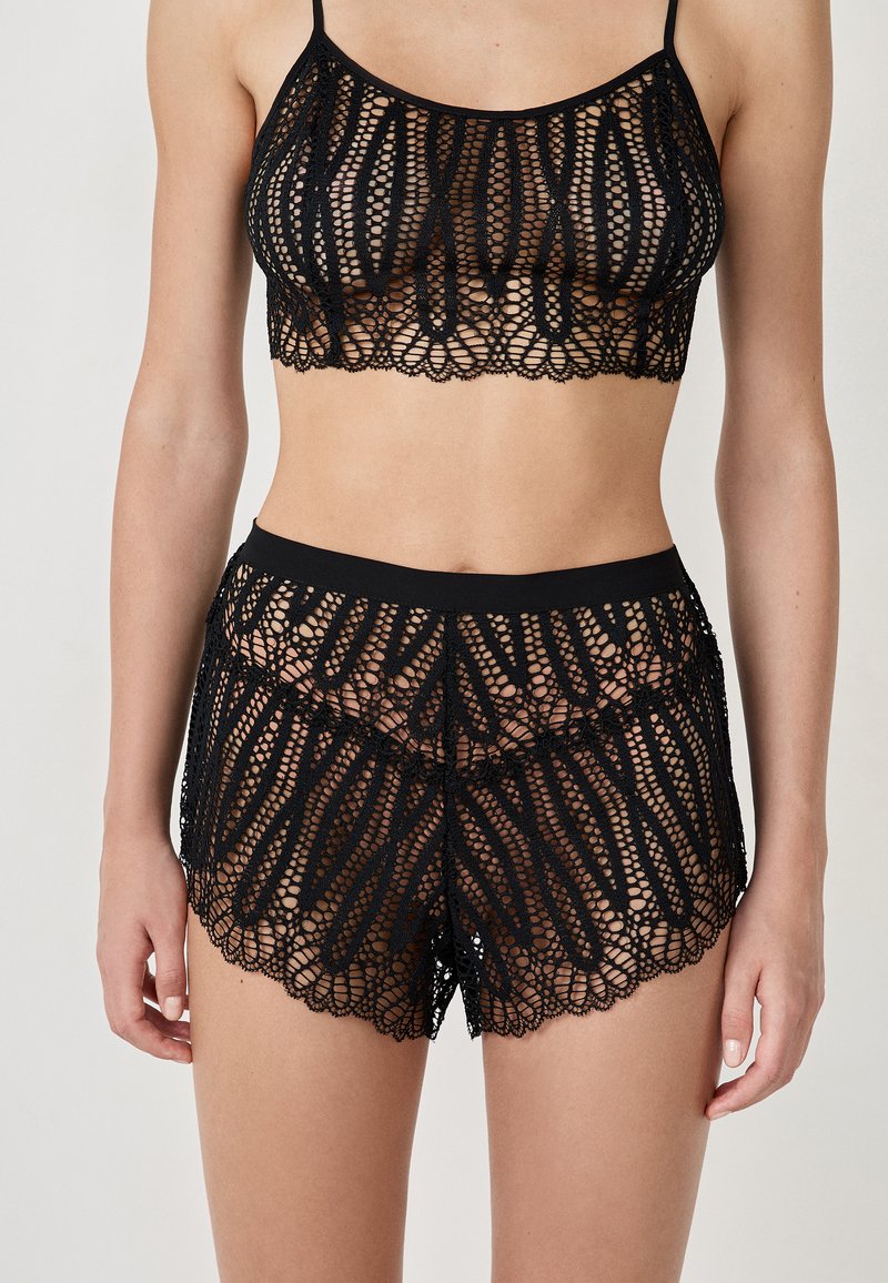 Zwarte kant bralette en bijpassende shorts met ingewikkelde uitsnijdingen, gekartelde randen en een zachte elastische tailleband.