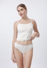 Witte camisole met dunne spaghettibandjes en een aansluitend lijfje, gecombineerd met bijpassende witte slipjes met kant, beide van een gladde stof.