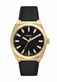 Montre en acier inoxydable doré avec un cadran texturé noir, des index horaires dorés et un bracelet en cuir noir. Présente une fenêtre de date à 6 heures.