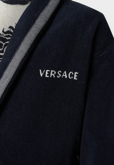 Μαύρο μπουρνούζι με υφή και λευκή κεντητική της "Versace" στο στήθος, με μια ματιά στην εσωτερική φόδρα με σχέδια.