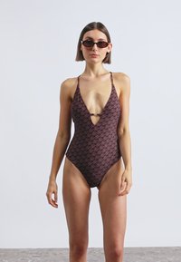Maillot de bain une pièce à encolure plongeante de couleur bordeaux foncé avec un motif clair répétitif. Comprend des bretelles fines et un découpage au niveau de la poitrine.