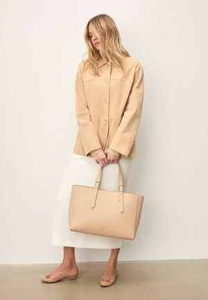 Beežist nahast õlakott lameda sangaga, sileda tekstuuri ja ristkülikukujuline. Kandmisega sobib beež jakk ja valge seelik.