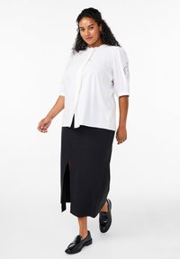 Vit skjorta med volangkrage och korta ärmar, matchad med en svart maxi kjol med en framklippning och bärs med svarta loafers.