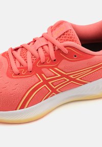 Koralle Sport Schuh mit Mesh-Obermaterial, kontrastierenden gelben Akzenten, flachen Schnürsenkeln, gepolstertem Kragen und flexibler Gummisohle.