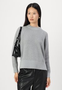 Maglione a maglia grigio chiaro con polsini e orlo a costine, caratterizzato da un colletto a girocollo e maniche raglan, abbinato a pantaloni in pelle nera e una borsa.