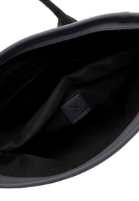 Svart toteväska med en slät yta, försedd med ett flätat handtag och ett innerfoder av svart tyg. Inkluderar en liten läderlogo i form av en lapp.