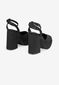 Zapatos de tacón negros con plataforma, tacón bloque grueso y correa al tobillo. Textura de tela suave y diseño de punta redonda. Característica de hebilla ajustable.
