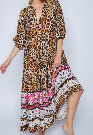 Kobieta ubrana w luźną sukienkę w panterkę z wzorami serc i kwiatów oraz napisem „Love & Peace” wzdłuż dołu, lekko podnosząca jedną stronę.