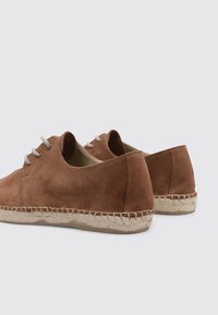 Zapatos de ante marrón con un diseño de corte bajo, con cordones gris claro y una suela de yute trenzado. Textura suave, punta redondeada, estilo minimalista.