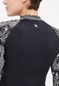 Crni sportski top s uzorkovanim rukavima koji sadrže geometrijske dizajne u bijeloj boji. Glatka tekstura i prilagođeni dizajn, s logotipom na leđima.