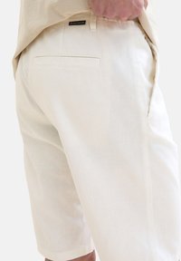 Light cream shorts in a soft, textured fabric, featuring side pockets and a subtle brand label on the back. Tailored cut for comfort.