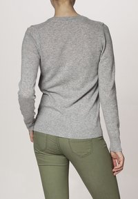 Pull en gray tricoté avec de longues manches, un col rond et une finition côtelée, associé à un pantalon vert ajusté. Texture douce et design minimaliste.