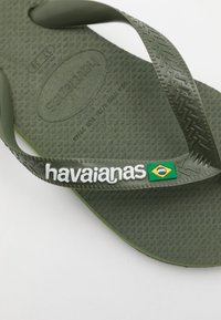 Zeleni gumeni natikači z dvignjeno podplatom, gumijastim trakom z logotipom "havaianas" in majhnim detajlom brazilske zastave.