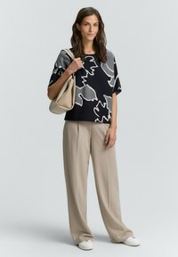 Czarny sweter z szarym abstrakcyjnym wzorem, w połączeniu z beżowymi spodniami szerokimi u dołu i białymi trampkami. Zawiera kremową torbę.