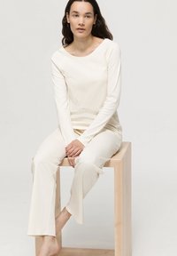 Krämfärgad loungeklädesset gjort av mjukt tyg. Långärmad topp med vid halsringning som matchas med löst sittande byxor. Slät textur.