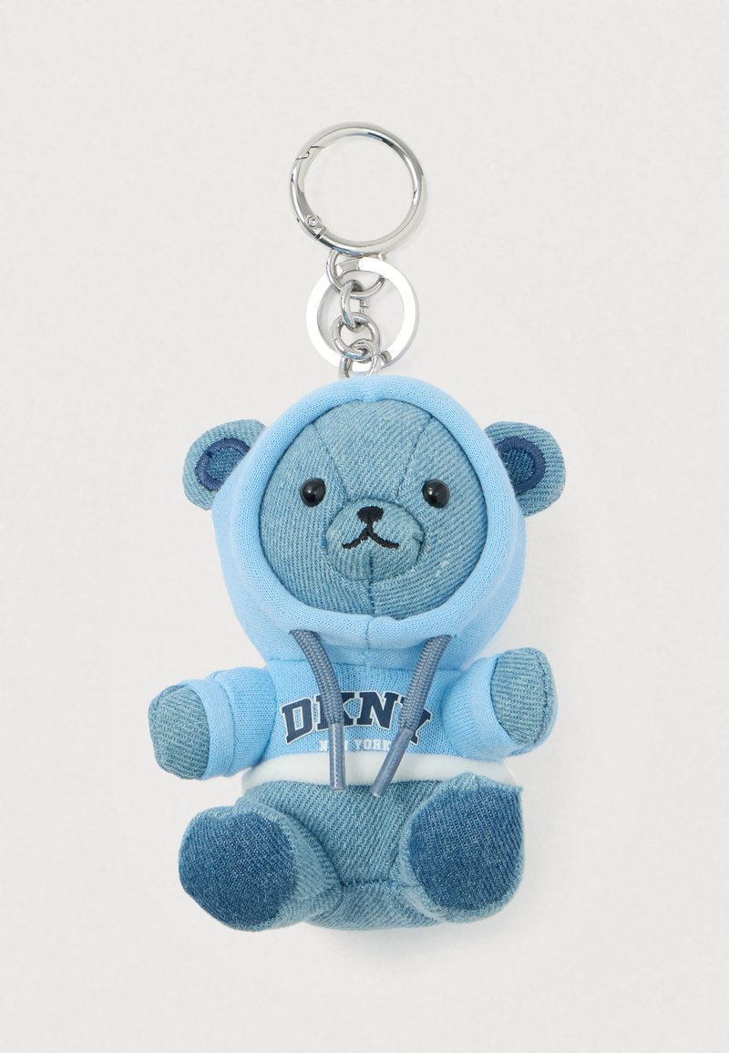 Chaveiro de urso de pelúcia em denim azul, vestindo um hoodie azul claro com o texto "DKNY New York", preso a um anel de chave prata sobre um fundo branco.