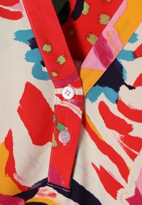 Farverig bomulds skjorte med et livligt abstrakt mønster i rød, pink, blå og grøn, med klassisk krave og hvide knapper.