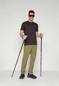 Fekete rövid ujjú póló, khaki nadrág és fekete cipő. Túrabotokat tart, sötét napszemüveget visel. Egyszerű dizájn, minimális márkázással.