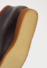 Bota de tobillo de cuero marrón con una suela plana de color claro. El borde presenta una transición suave de tonos oscuros a claros.