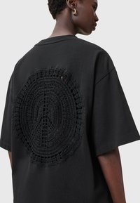 Sort oversized T-shirt med korte ærmer, der har et cirkulært hæklemønster på ryggen, hvilket skaber et tekstureret åbent detalje.