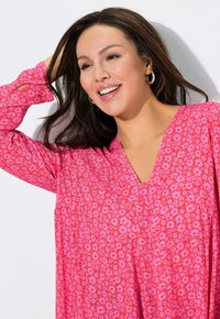 Růžový top s květinovým vzorem, výstřihem do V a dlouhými rukávy. Má volný střih a lehkou látku, zdobený malými květy v červené a růžové barvě.