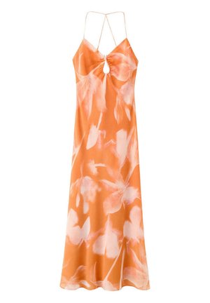Femme aux cheveux bouclés portant une robe dos nu orange et rose à fines bretelles et des sandales compensées noires, debout sur fond blanc.