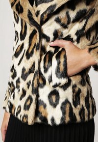 Leopardprint nepbontjas met een beige, zwarte en bruine patroon. Voorzien van een knoopsluiting en zijzakken. Zachte textuur en gezellige uitstraling.