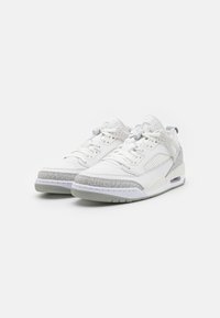 Valkoiset tennarit, joissa yhdistyvät nahka ja verkkokangas. Pohjassa harmaa kuvioitu koriste, ja kenkä on virtaviivainen. Nauhallinen kiinnitys.