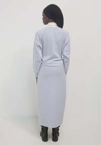 Langes graues Kleid aus weichem Stoff mit langen Ärmeln und lockerer Passform, kombiniert mit schwarzen Schnürstiefeln, von hinten betrachtet.