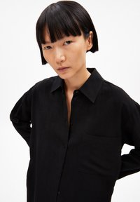 Schwarzes Hemd mit Knopfverschluss, Kragen, langen Ärmeln und einer Brusttasche. Hat einen lässigen Schnitt und eine glatte Textur.