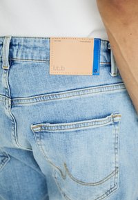 Svetlo modri denim kavbojki z našitimi žepi, ki imajo na hrbtnem pasu rjave usnjene oznake z modrimi detajli in napisom "l.t.b".