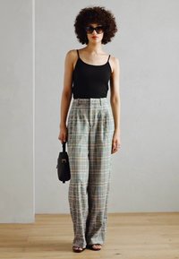 Schwarzes Tanktop, karierte weite Beinhosen in Pastellfarben, glatter Stoff, hohe Taille, kombiniert mit schwarzen Sonnenbrillen und einer kleinen Handtasche.