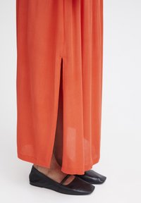 Lång, flödande orange kjol med en sidoinsnitt, gjord av lätt tyg. Kombinerad med enkla svarta ballerinas. Slät textur och avslappnad design.