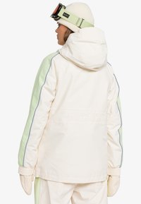 Hvid og lys grøn isoleret jakke med hætte, udstyret med elastiske ærmer, vandafvisende materiale og "ROXY" logo broderi på ryggen.