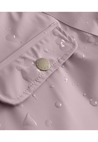 Tessuto rosa resistente all'acqua con una texture liscia, dotato di una tasca a patta e di un logo circolare dorato. La superficie mostra gocce d'acqua.
