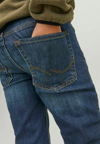 Mörkblå denimjeans med en ficka som har kontrasterande sömmar och en lätt sliten yta. Passformen svänger något vid benen.