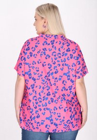 Maglietta a maniche corte di un brillante colore rosa con stampa leopardata blu, dotata di una vestibilità rilassata e tessuto morbido, bordi orlati e spacchi laterali.