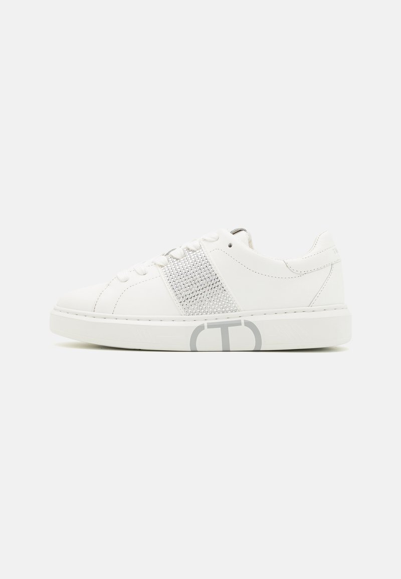 Sneaker bianco con tomaia in pelle liscia, pannello in rete e dettagli argentati. Presenta punta rotonda, design con lacci e logo sulla suola.