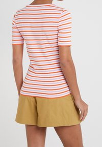 Pruhovaný krátký rukáv top v bílé, růžové a oranžové barvě s kulatým výstřihem. Spárováno s khaki šortkami, které mají uvolněný střih a jemnou texturu.