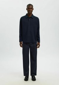 Mornarsko modra polo majica z dolgimi rokavi in ovratnikom, v kombinaciji s temno prugastimi hlačami in črnimi čevlji, z udobnim krojem in teksturirano tkanino.